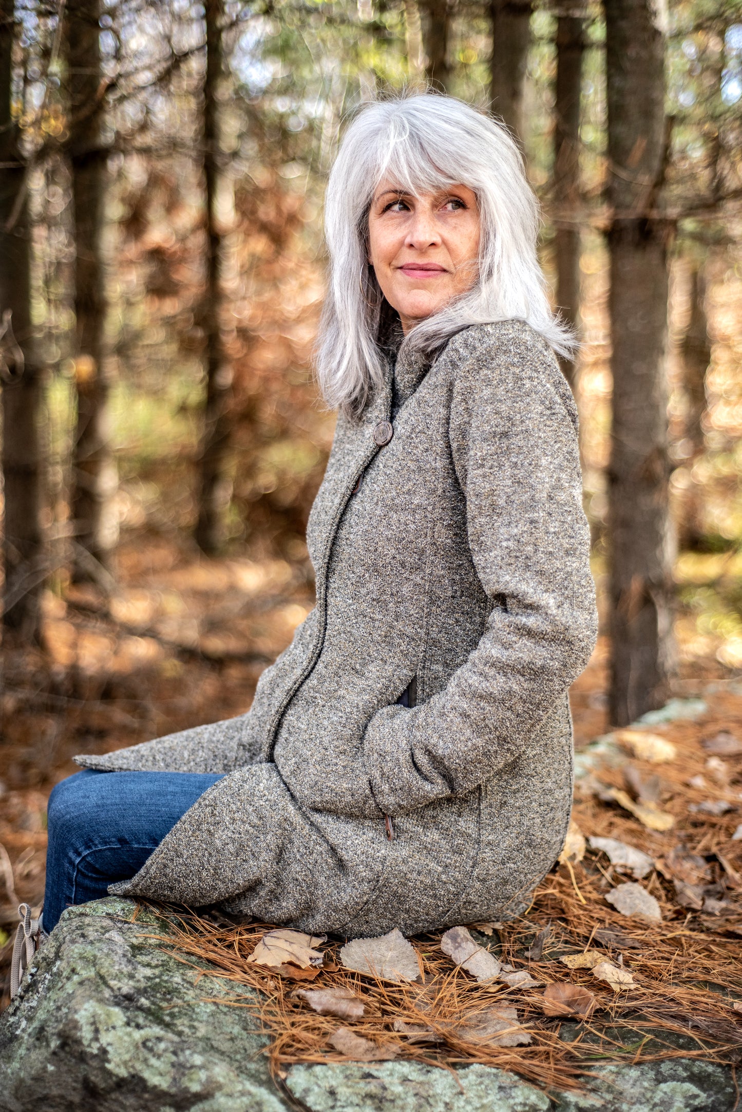 A woman smiles while looking off into the distance, as she sits on a rock in South Frontenac, ON
