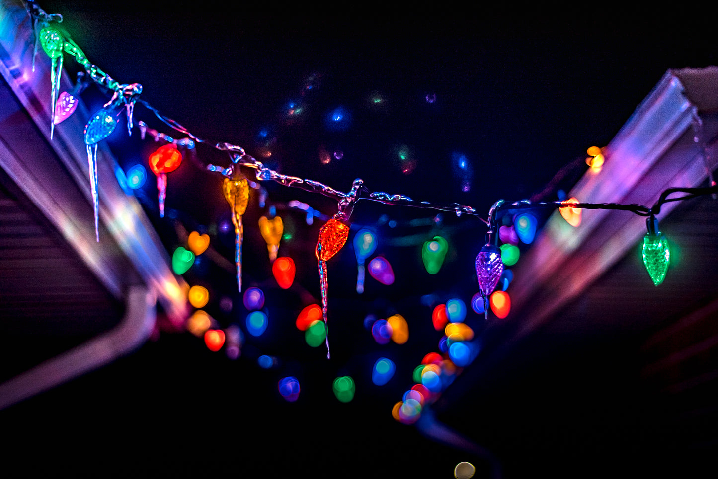 Icicles cover lights while they hang above a porch, on a roof