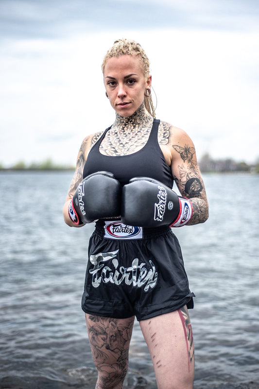 A tattooed woman shows off her fighting stance in boxing gloves